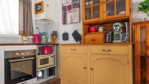 A kitchen with a De'Longhi oven, a microwave, and a toaster. There are wooden cabinets with glass doors and a plant on the right. - Unit 1 - A welcoming and cosy unit, near Wanda beach and Cronulla Golf Course (Cronulla)