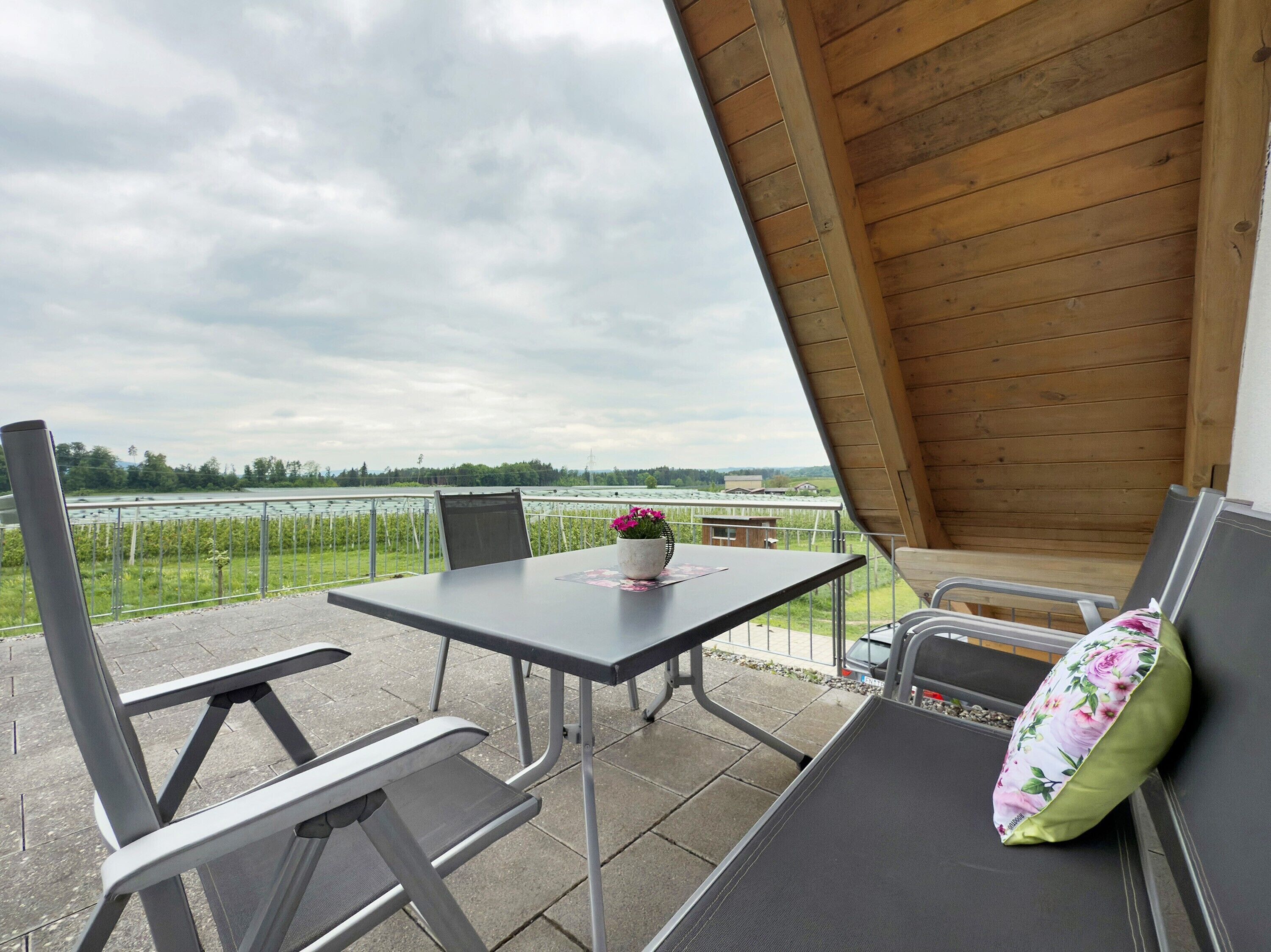 An outdoor patio with a table and chairs, a flower vase, and a view of a lake.