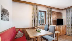 Een knus interieur met een houten plafond, een eettafel met stoelen, een rode bank, een televisie en een raam met gordijnen.