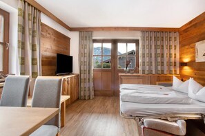 Habitación de hotel con detalles de madera, una cama, un escritorio con televisor y una ventana con cortinas.