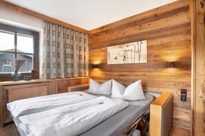 Habitación con paneles de madera, una cama, un ventanal con cortinas y un cuadro colgado en la pared.