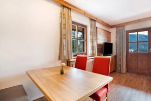Une pièce avec une table en bois, des chaises rouges, un téléviseur et des fenêtres avec des rideaux.
