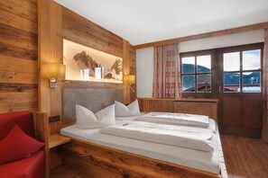 Ein Zimmer mit Holzboden, einem Bett, einem roten Sessel und einem Fenster mit Blick.