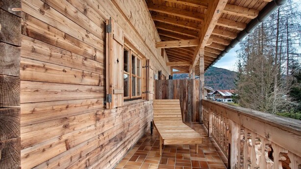 A wooden cabin with a covered porch, wooden walls, and a tiled floor.