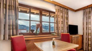 A room with a wooden table, red chairs, a TV, and a window with a view of mountains.
