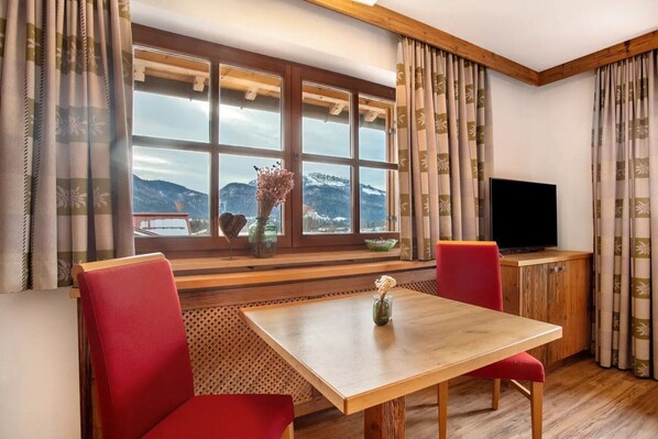 Una habitación con una mesa de madera, sillas rojas, un televisor y una ventana con vistas a las montañas.