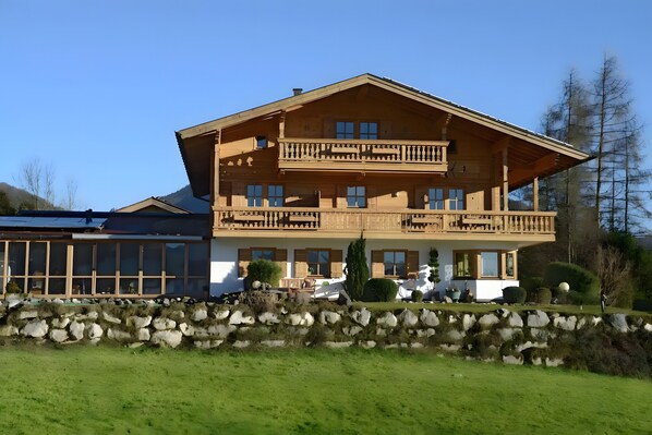 A two-story wooden building with balconies, a stone wall in front, and a clear sky.