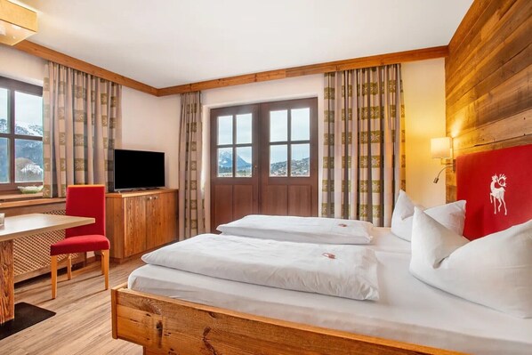 Ein Hotelzimmer mit einem Bett, einem Schreibtisch, einem Sessel, einem Fernseher und einem Fenster mit Vorhängen.