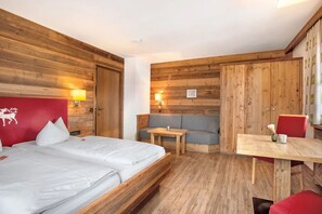 Ein Hotelzimmer mit einem hölzernen Kopfteil, einem Bett, einer Couch, einem kleinen Tisch und einem Esstisch.
