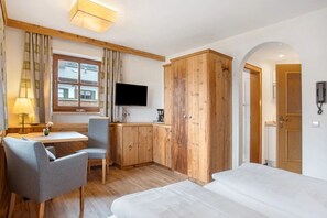 Hotellihuone, jossa on sänky, työpöytä tuolilla, televisio, puinen vaatekaappi ja ikkuna, jossa on verhot.