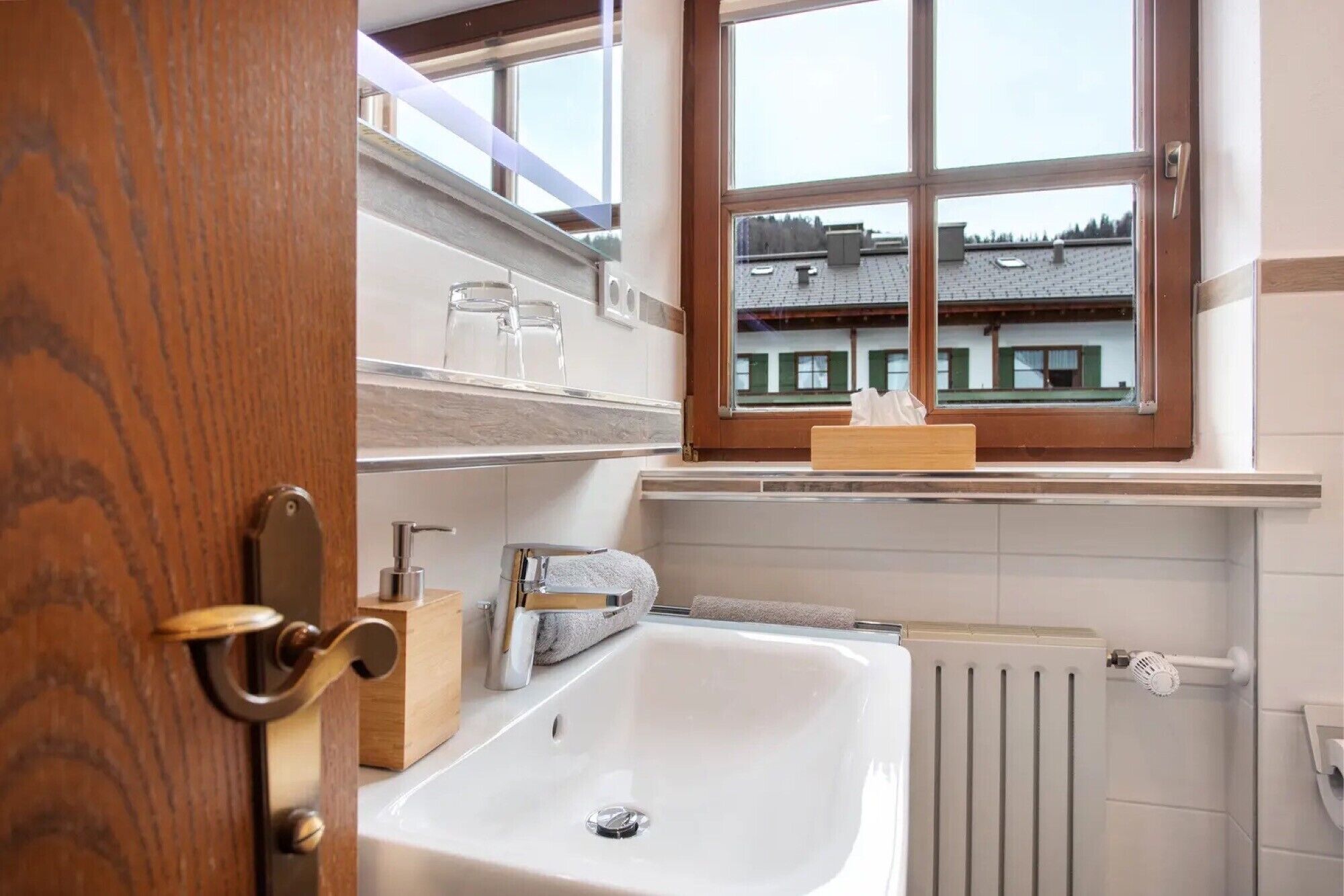 A bathroom with a white sink, a towel, a soap dispenser, and a window with a view of buildings.