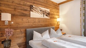 A hotel room with a wooden wall, a bed with white bedding, a nightstand with a lamp, and a framed picture. - Studio 'Gästehaus Panorama - Apartment 5' with Mountain View, Private Balcony & Shared Sauna (Reit im Winkl)