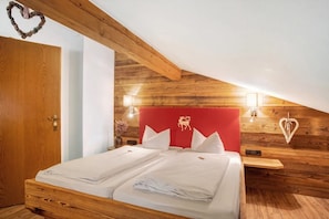 A bedroom with a wooden ceiling, a red headboard with a deer logo, white bedding, and two bedside tables with lamps.