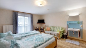 Une chambre d’hôtel avec un lit, un canapé, une télévision, une petite table, un lavabo et une fenêtre avec des rideaux.