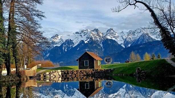 Eine Holzhütte an einem stillen See mit Bergblick.