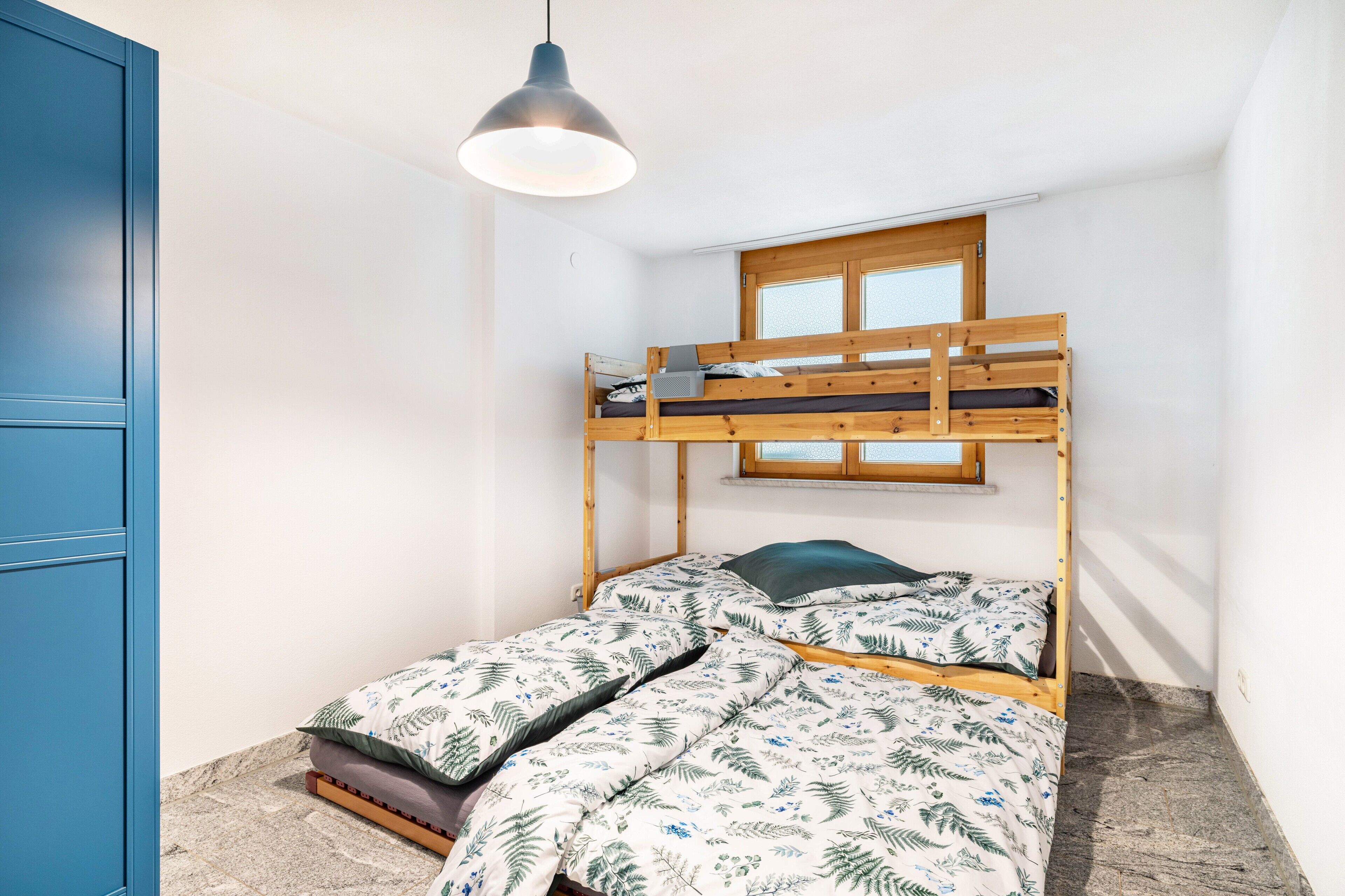 A bunk bed with a window above, a blue door, and a hanging light fixture.