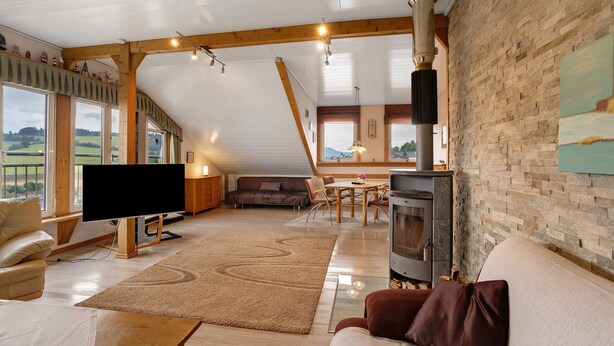 A spacious living area with a television, sofa, and fireplace, featuring large windows and a sloped ceiling. - Holiday Apartment 'Panoramablick' with Sauna, Mountain View, Private Terrace and Wi-Fi (Olsberg)