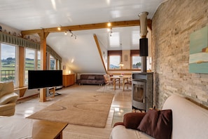 Amplia sala de estar con televisor, sofá y chimenea, que cuenta con ventanas amplias y un techo inclinado.