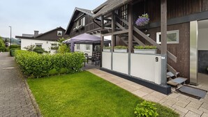 A modern building with a wooden facade, a covered outdoor seating area, and a well-maintained lawn. - Holiday Apartment 'Panoramablick' with Sauna, Mountain View, Private Terrace and Wi-Fi (Olsberg)