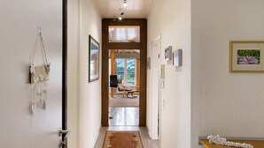 A hallway with a wooden door, a welcome sign, framed pictures, and a view into a room with a chair and window. - Holiday Apartment 'Panoramablick' with Sauna, Mountain View, Private Terrace and Wi-Fi (Olsberg)