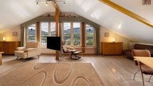 A spacious attic bedroom with a large window, a flat-screen TV, a wooden ceiling, and a cozy seating area. - Holiday Apartment 'Panoramablick' with Sauna, Mountain View, Private Terrace and Wi-Fi (Olsberg)
