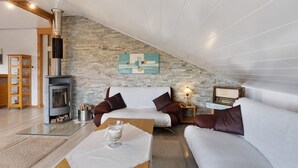 A cozy living room with a stone wall, a fireplace, a sofa, a coffee table, and a lamp. - Holiday Apartment 'Panoramablick' with Sauna, Mountain View, Private Terrace and Wi-Fi (Olsberg)