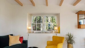 A room with a dark green sofa, a yellow armchair, a small round table, a window with curtains, a potted plant, and a wooden ceiling beam. - Holiday Home 'Backhaus' with Mountain View, Private Terrace and Private Garden (Lauterbach)