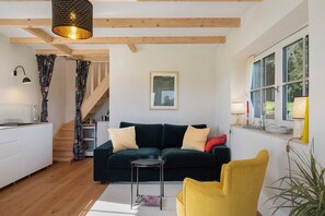 Una sala de estar moderna con un sofá verde oscuro, un sillón amarillo, una pequeña mesa redonda y una escalera que conduce a otro nivel.