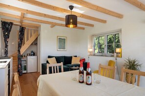 Una habitación acogedora con una mesa de comedor, dos botellas de vino, un refrigerador pequeño, un sofá y una ventana con vistas al verdor.