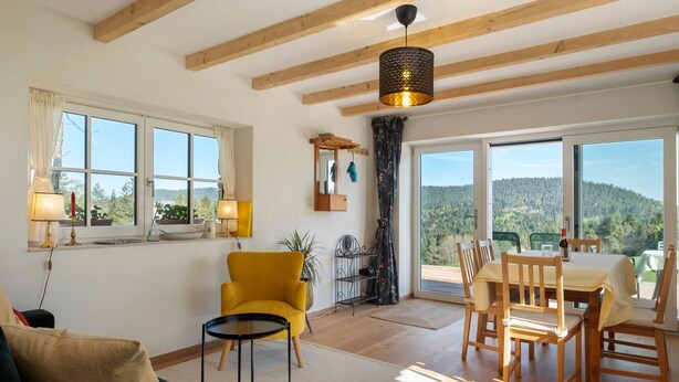 A room with a dining table, chairs, a sofa, a yellow armchair, a lamp, and a view of the outdoors. - Holiday Home 'Backhaus' with Mountain View, Private Terrace and Private Garden (Lauterbach)