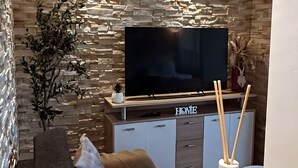 A modern living room with a stone wall, a flat-screen TV, a sofa, a coffee table, and a decorative vase.