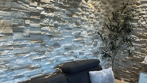 A modern living room with a stone wall, a dark sofa with cushions, and a clock.