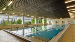 An indoor swimming pool with clear windows, wooden ceiling, and tiled floor.