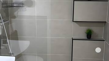 Un baño moderno con ducha, lavamanos y dos plantas en macetas sobre estantes.