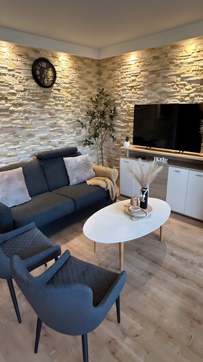 A modern living room with a stone wall, a sofa, a coffee table, and a TV. - Superior Apartment 229 with Pool and Sauna (Braunlage)