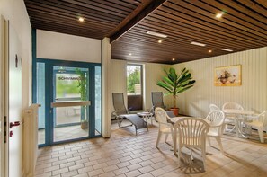 A covered patio area with a wooden ceiling, outdoor seating, and a view through a glass door. - Superior Apartment 229 with Pool and Sauna (Braunlage)