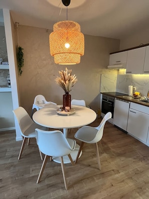 A modern kitchen with white cabinets, a round dining table with white chairs, a hanging wicker light fixture, and a vase with dried flowers. - Superior Apartment 229 with Pool and Sauna (Braunlage)