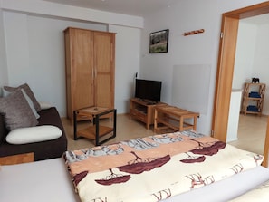 Una habitación con sofá, armario de madera, televisor, mesita y cama con colcha estampada.