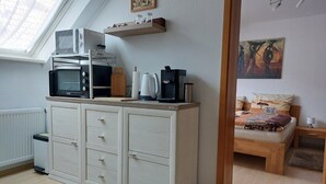 Un dormitorio con una cama, una mesita de noche, un aparador de madera, un microondas, un tostador y un cuadro en la pared.