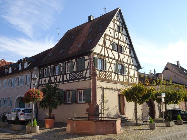 A traditional half-timbered house with a courtyard, a well, and potted plants.