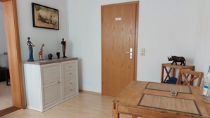 Una habitación con una mesa de comedor de madera, un mueble con cajones, una puerta de madera con la etiqueta 'WC' y un cuadro colgado en la pared de una vaca.