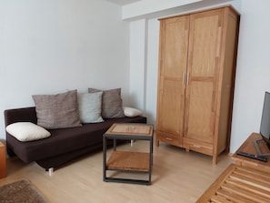 Una sala de estar con un sofá marrón oscuro, un mueble de madera y una mesita con tapa de mimbre.