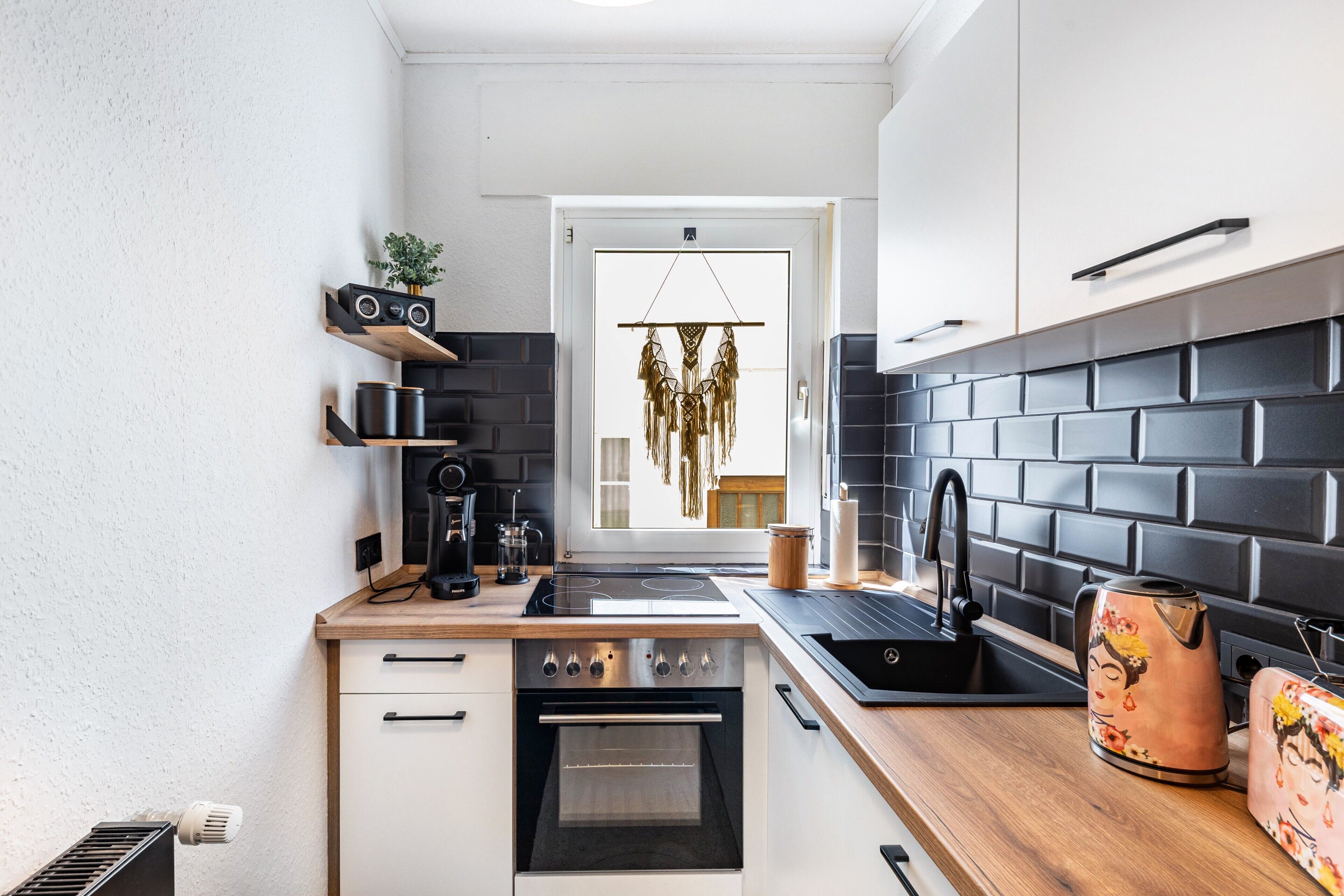 Een moderne keuken met een zwart betegelde spatwand, houten aanrecht, een ingebouwde oven en een koffieapparaat.