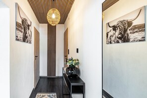 A hallway with wooden slats on the ceiling, a black console table with a vase of flowers, and two framed pictures of a yak on the walls. - Apartment 54 'Unit 1' with Private Terrace (Homberg (Efze))
