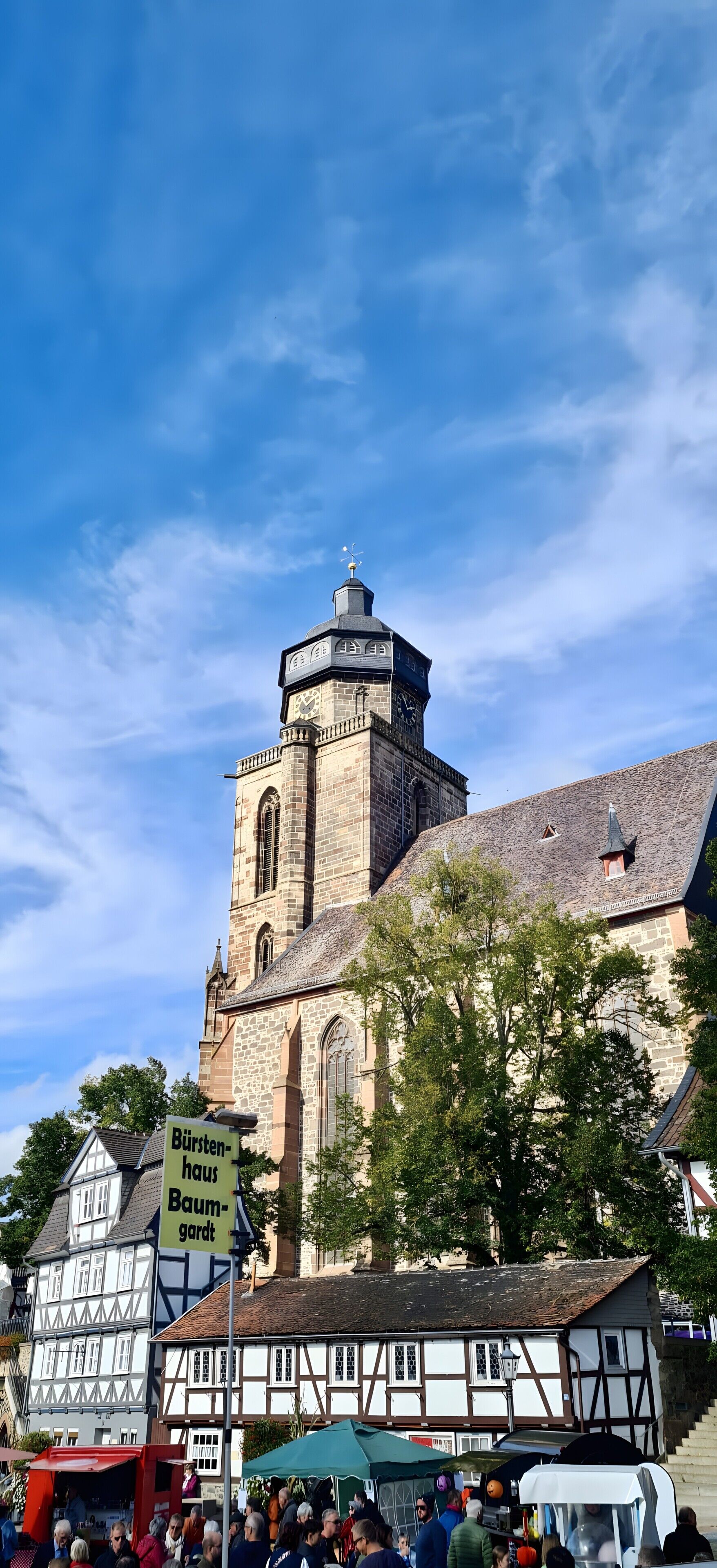 Una chiesa storica con una torre imponente e un cartello con la scritta 'Bürstenhaus Baumgarten' di fronte.