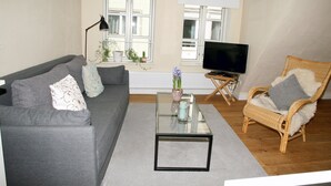 Una sala de estar con sofá, sillón, mesa de centro, televisor y ventanas.