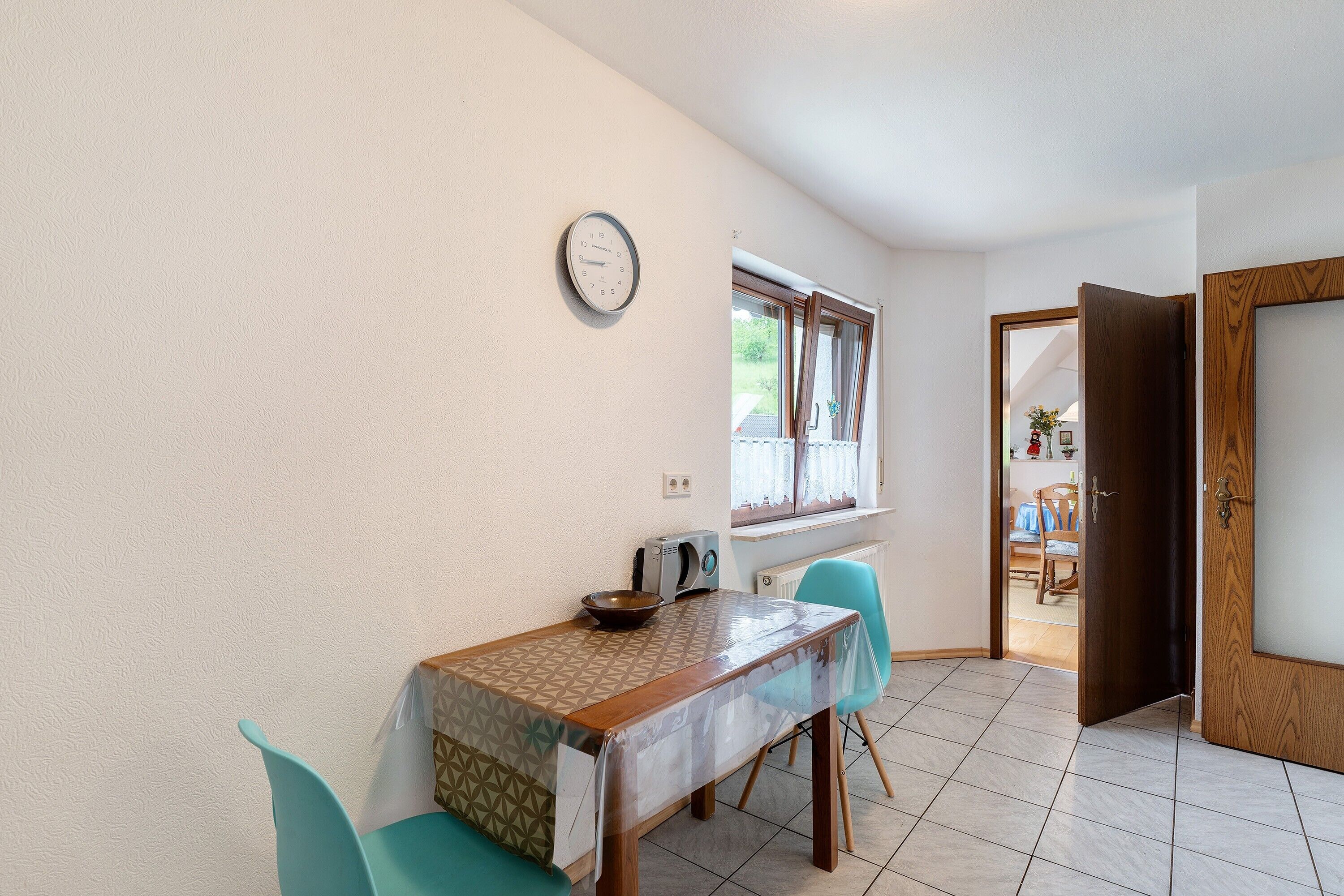 A dining area with a table, chairs, a clock, and a window.