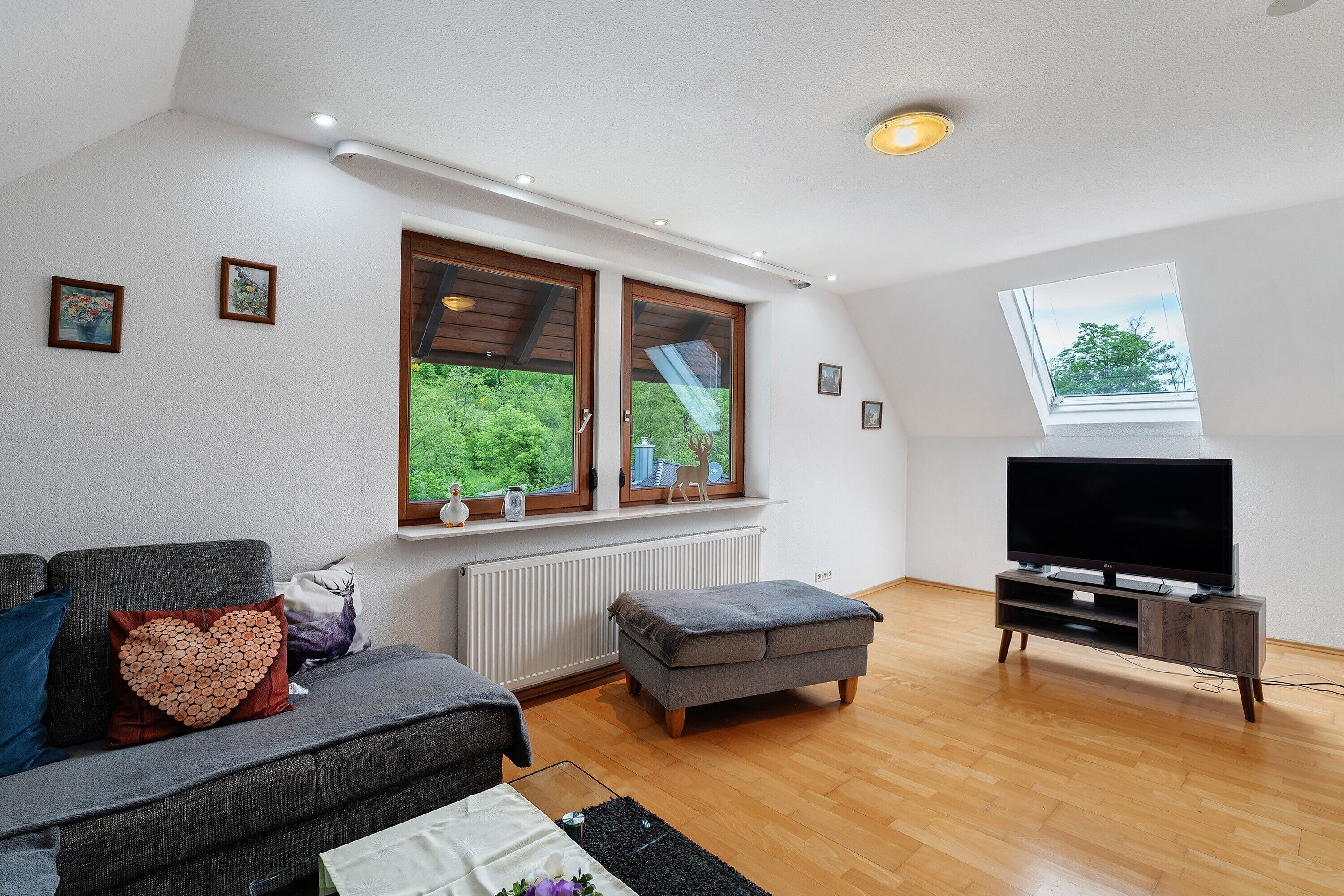 Una sala de estar con sofá, reposapiés, mueble para televisión y tragaluz.