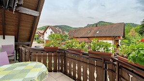 Ein Balkon mit einem karierten Tisch, Holzgeländer und Topfpflanzen.