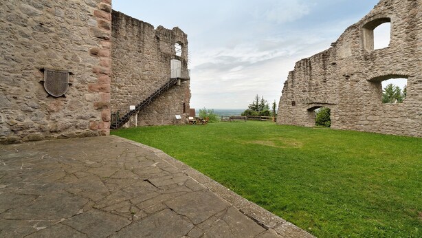 Ein steinerner Innenhof mit Ruinen, einer Treppe und einer Rasenfläche.